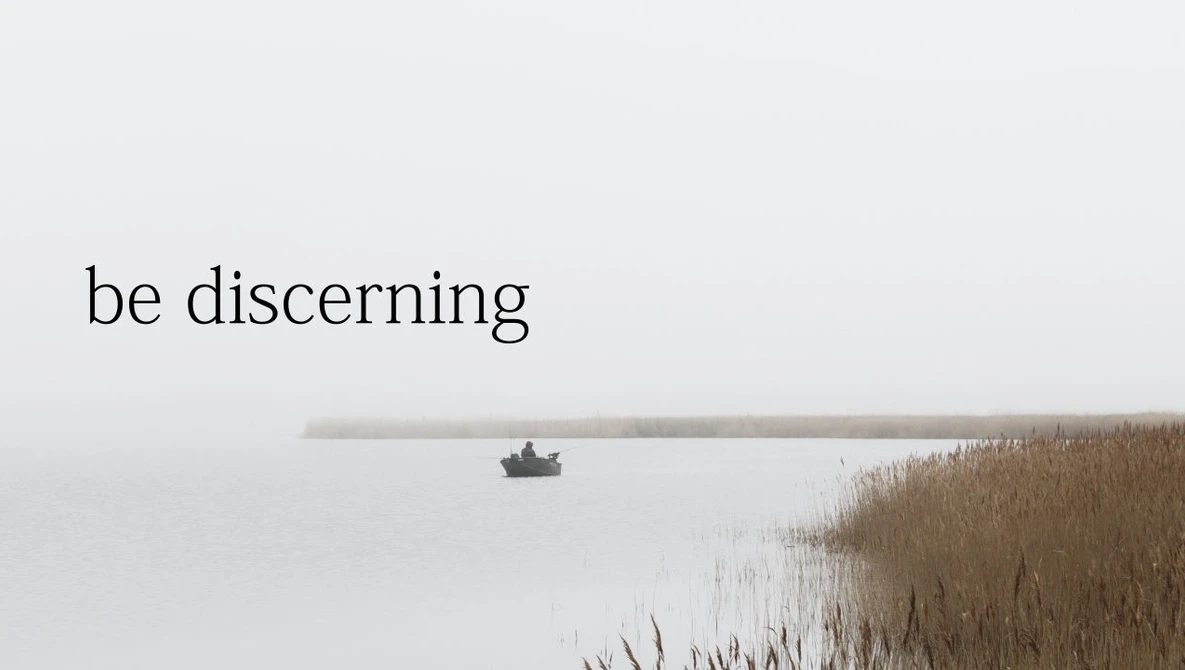Small fishing boat on calm, misty water with dry reeds along the shore.