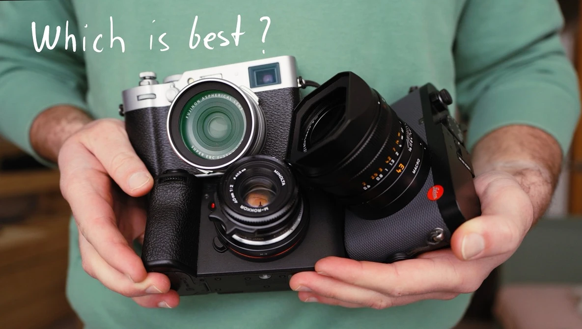 Hands holding a rangefinder camera with interchangeable lens and accessories, posed against a green shirt.