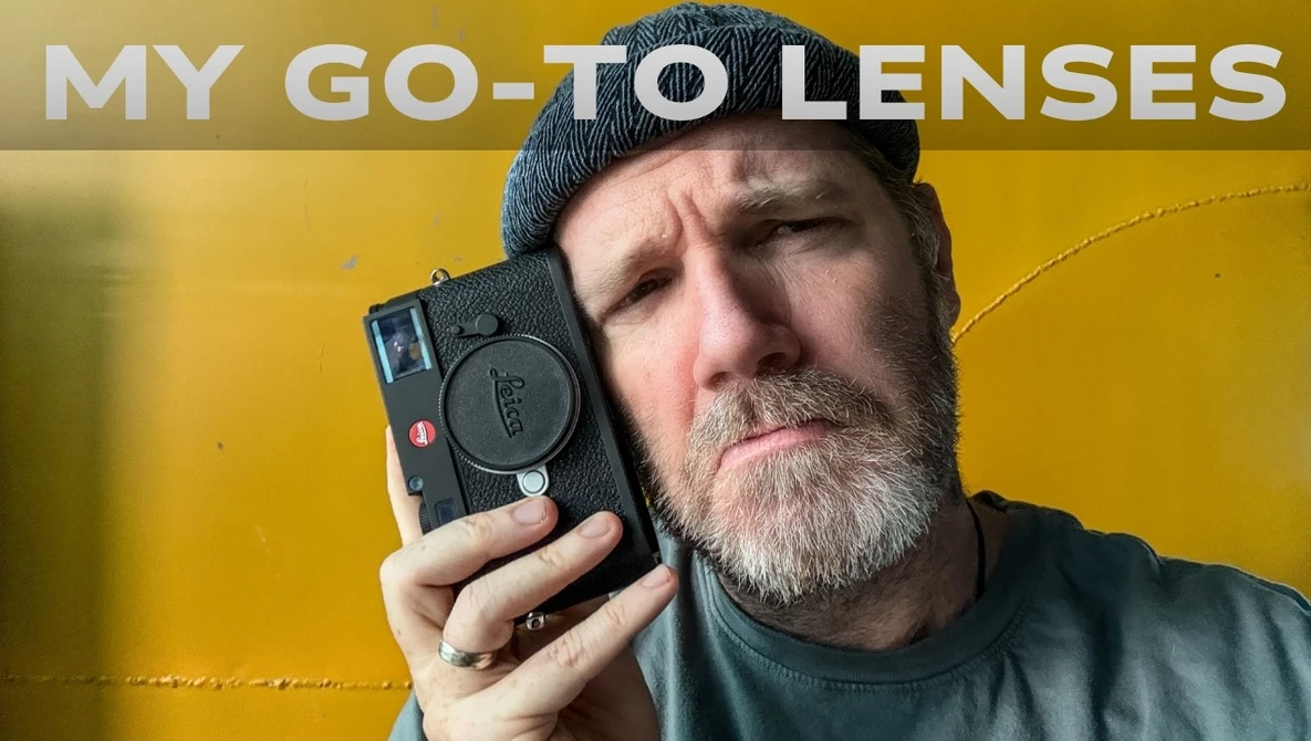 Photographer holding a compact rangefinder camera against a yellow background.
