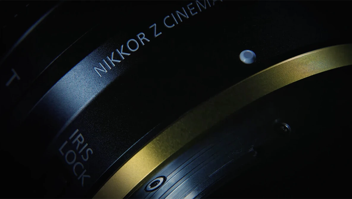 Close-up of a Nikkor Z Cinema lens with focus ring and depth of field markings visible against dark background.