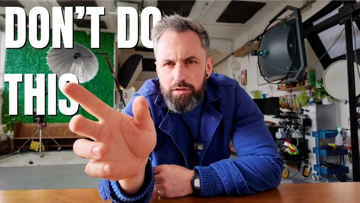 Videographer in blue jacket gesturing toward camera in studio setting with warning text overlay.