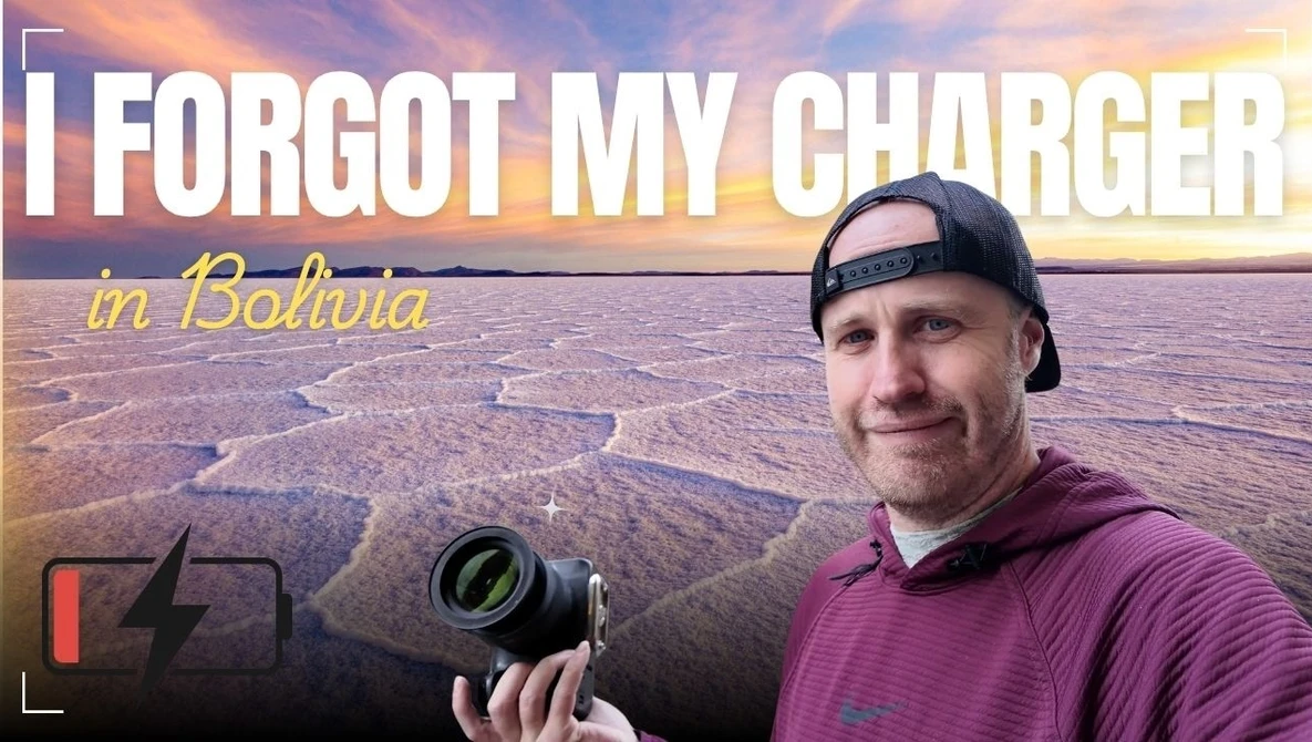 Photographer holding a camera with a depleted battery indicator, standing in front of a vast salt flat at sunset.