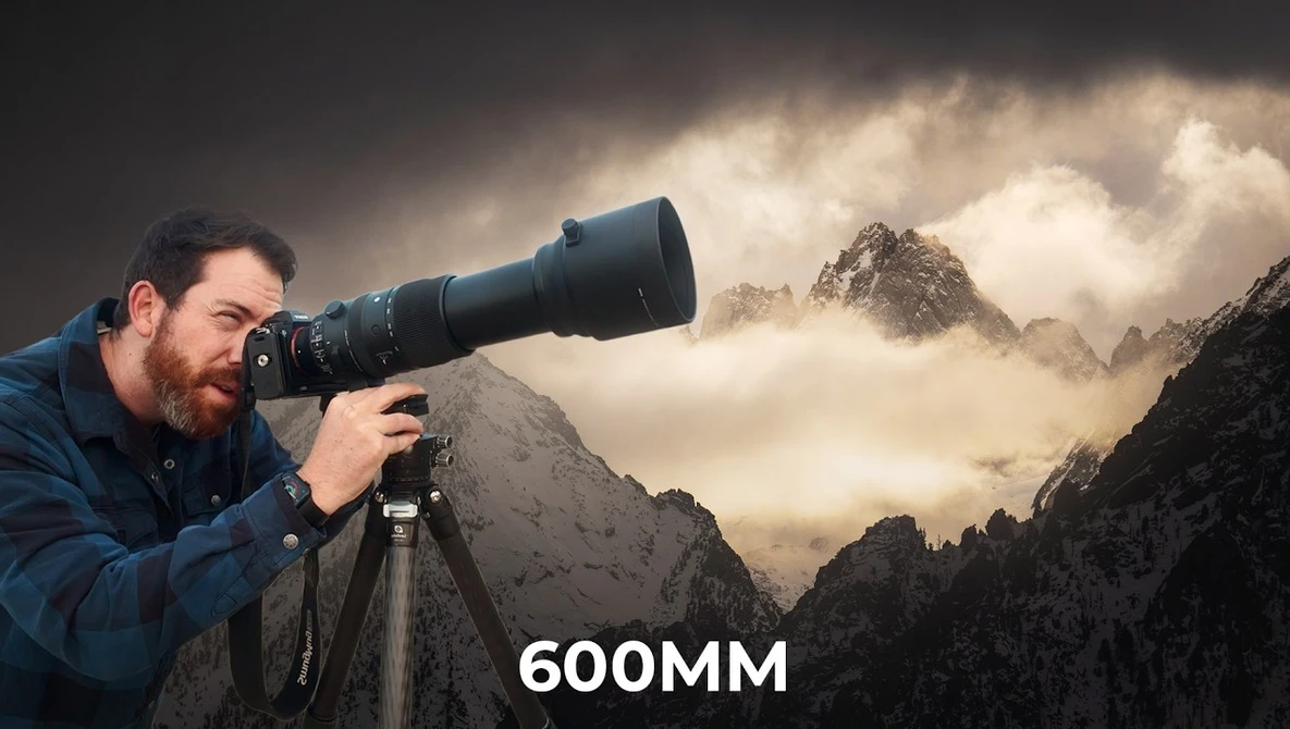 Photographer with 600mm telephoto lens on tripod, aiming at misty mountain peaks.