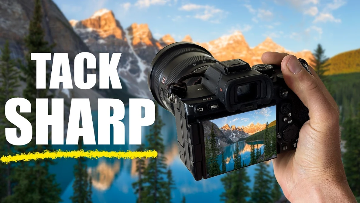 Hand holding a mirrorless camera displaying a sharp landscape photo of a mountain lake on its rear screen.