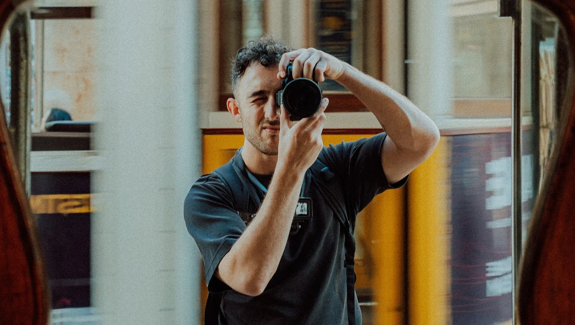 Male photographer looking through camera viewfinder in indoor space.