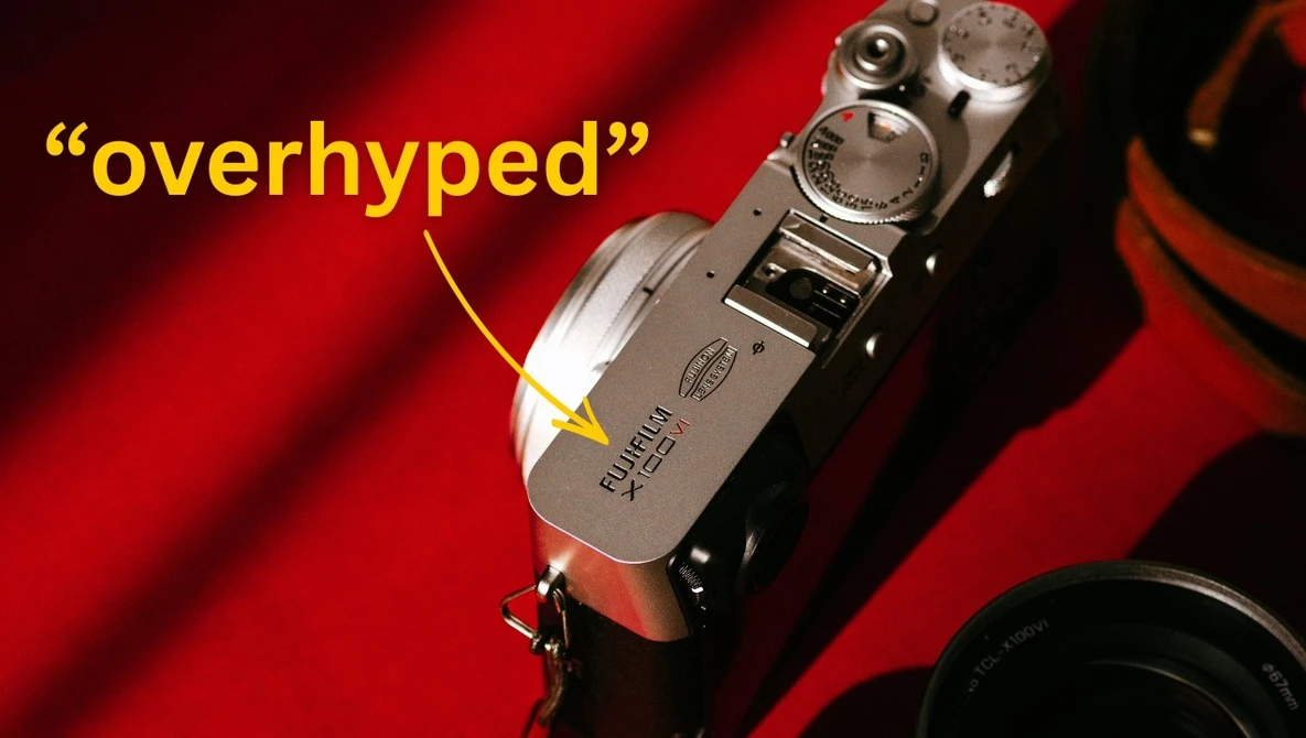 Vintage rangefinder camera with dials and controls on red fabric background with 'overhyped' label.