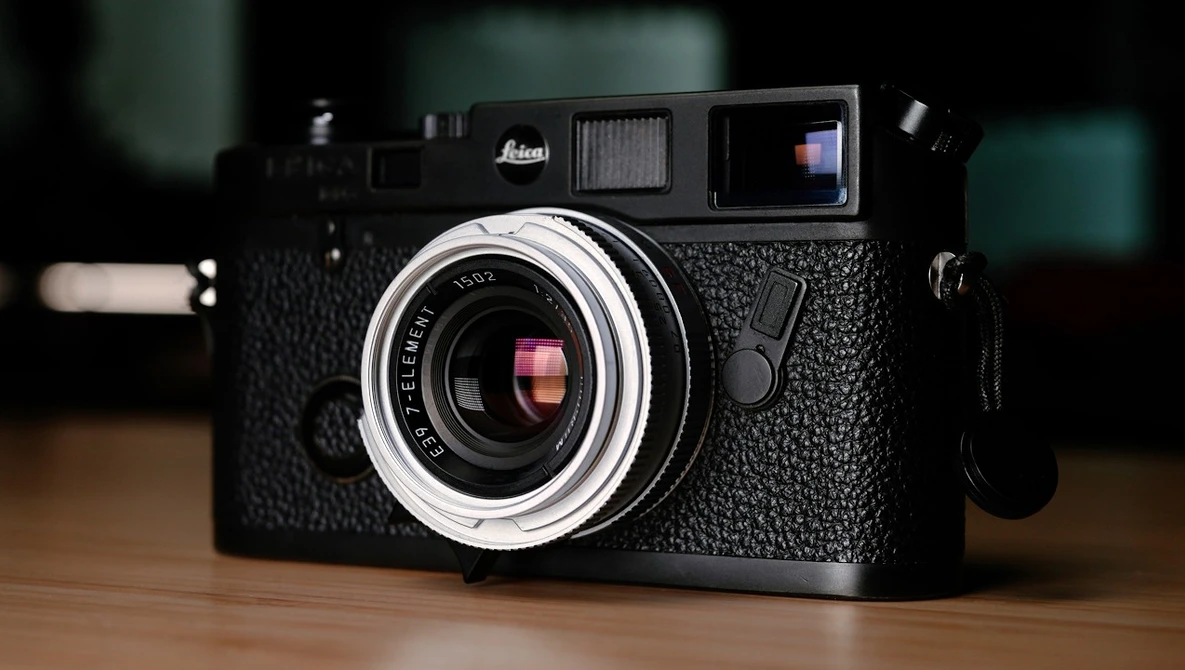 Black Leica rangefinder camera with chrome lens and textured body on wooden surface.