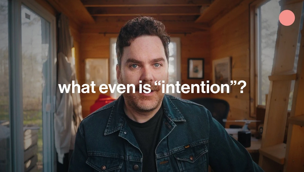 Man in denim jacket with skeptical expression in warm-toned wooden hallway.