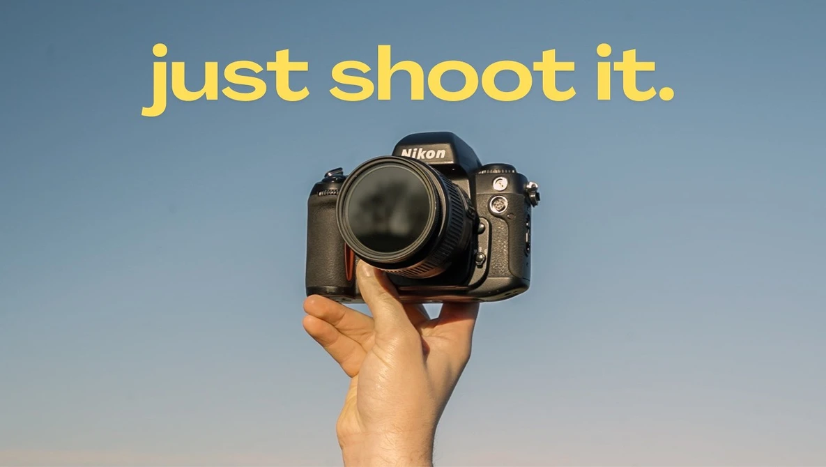 Hand holding a Nikon DSLR camera against a clear blue sky.