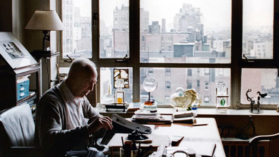 Man working at typewriter at desk overlooking urban skyline through large windows