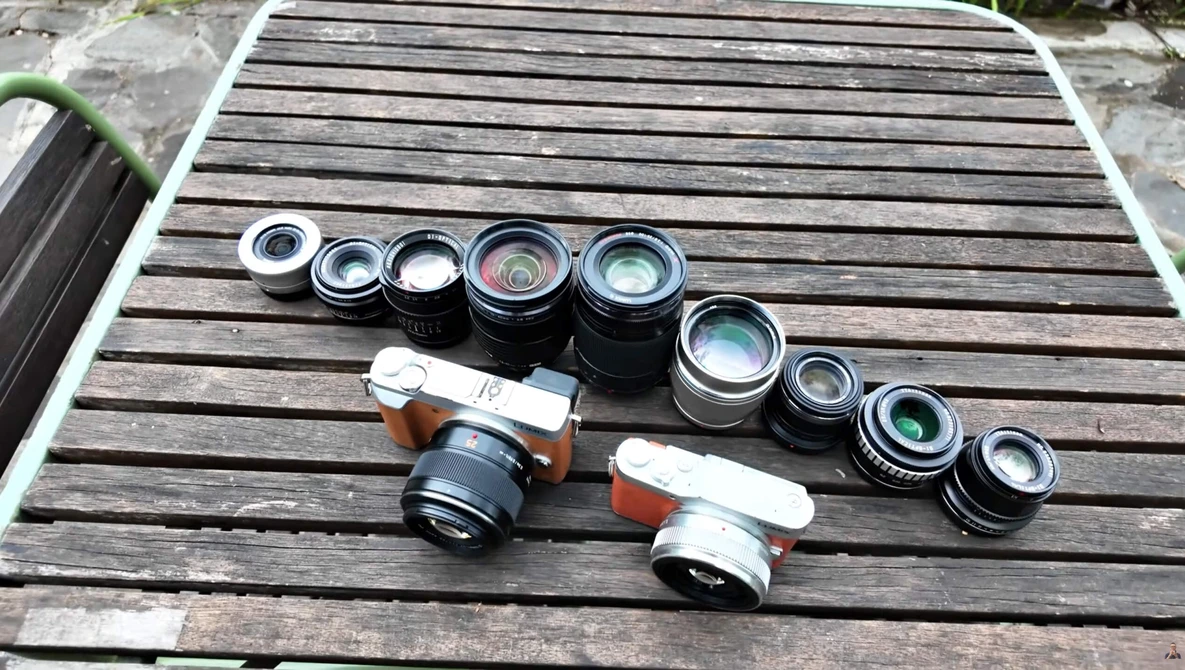 Collection of vintage rangefinder camera lenses and two film camera bodies arranged on wooden surface