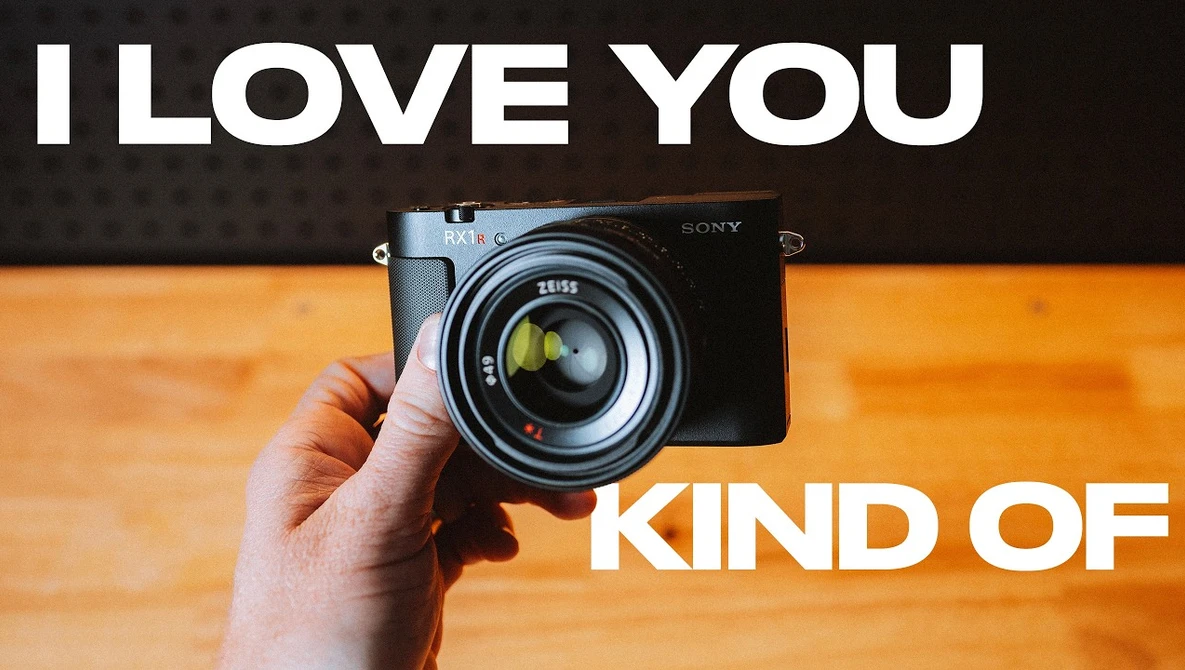 Hand holding Sony mirrorless camera with Zeiss lens against orange wooden surface