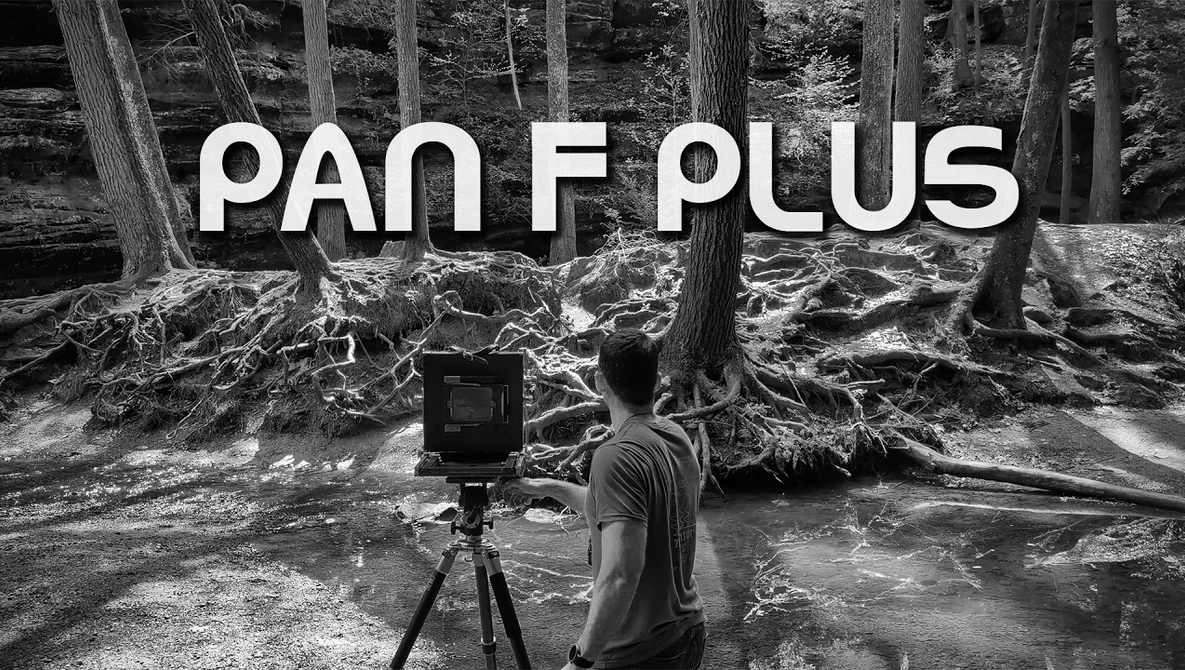 Photographer operating a camera on tripod in a forested stream setting