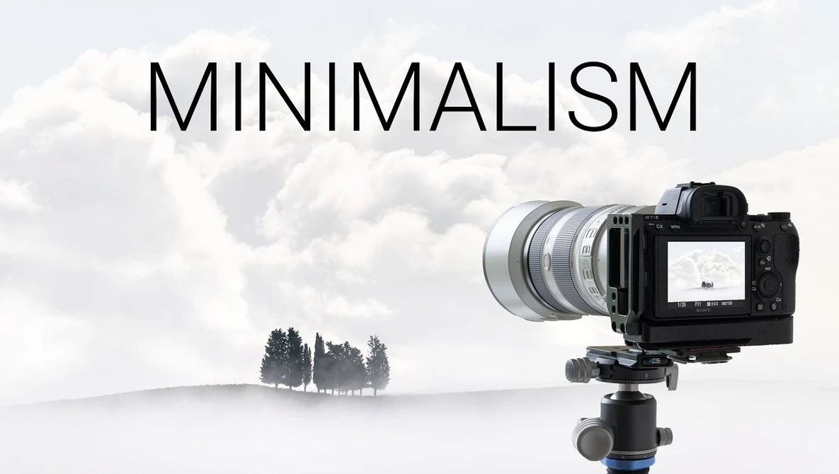 Mirrorless camera on tripod with telephoto lens pointed at minimalist landscape with three trees
