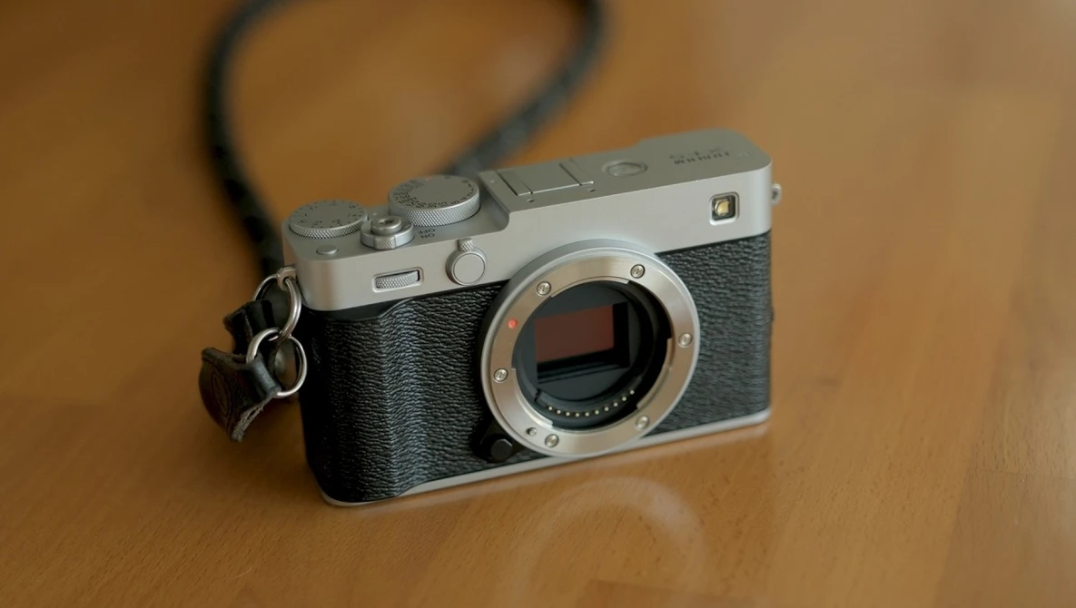 Rangefinder camera with chrome top plate and black leather body, displayed on wooden surface with shoulder strap