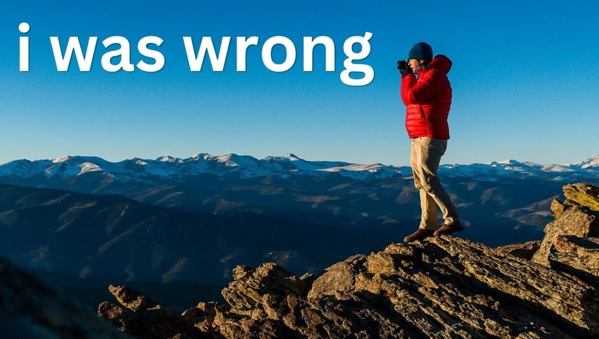 Person in red jacket standing on mountain peak overlooking alpine landscape