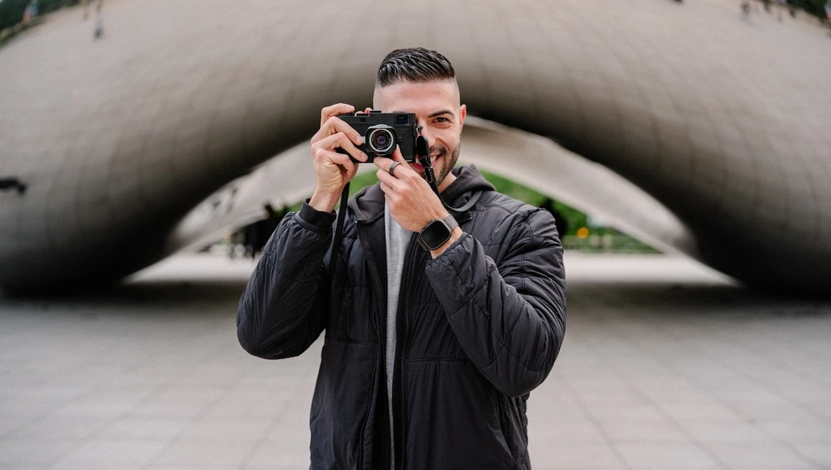 Photographer holding rangefinder camera to face while standing in front of curved concrete architectural structure