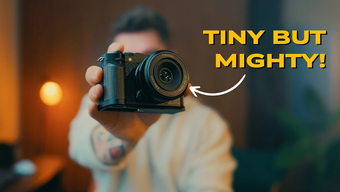 Photographer holding a compact mirrorless camera toward the viewer with overlaid text reading 'TINY BUT MIGHTY!'