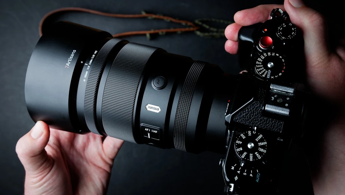 Photographer's hands holding mirrorless camera with telephoto lens against dark background