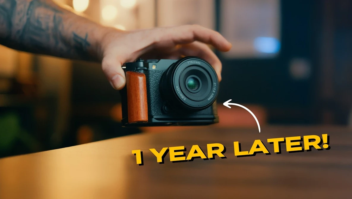 Hands holding a compact mirrorless camera with orange accent grip on wooden table