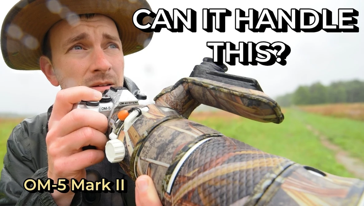 Photographer in cowboy hat holding OM-5 Mark II camera with large telephoto lens in muddy field
