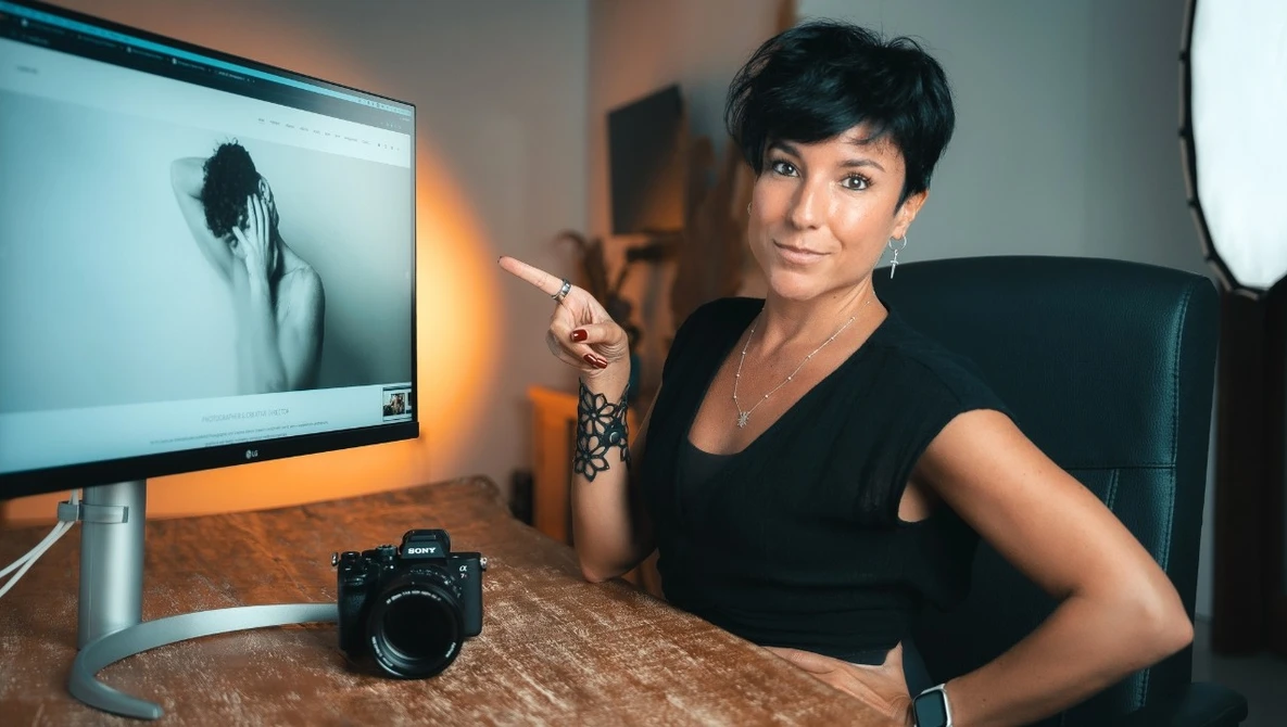 Female photographer at desk reviewing portrait on monitor with professional camera in foreground