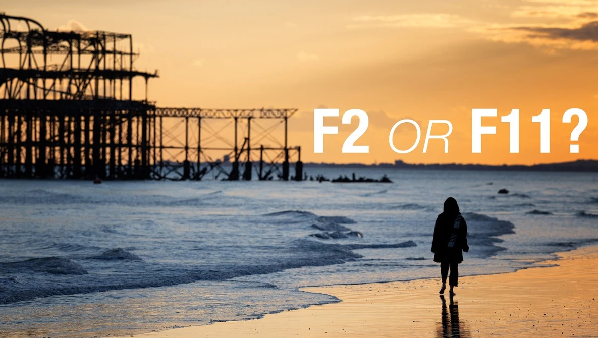 Silhouetted figure wading in ocean at sunset with abandoned pier structure in background