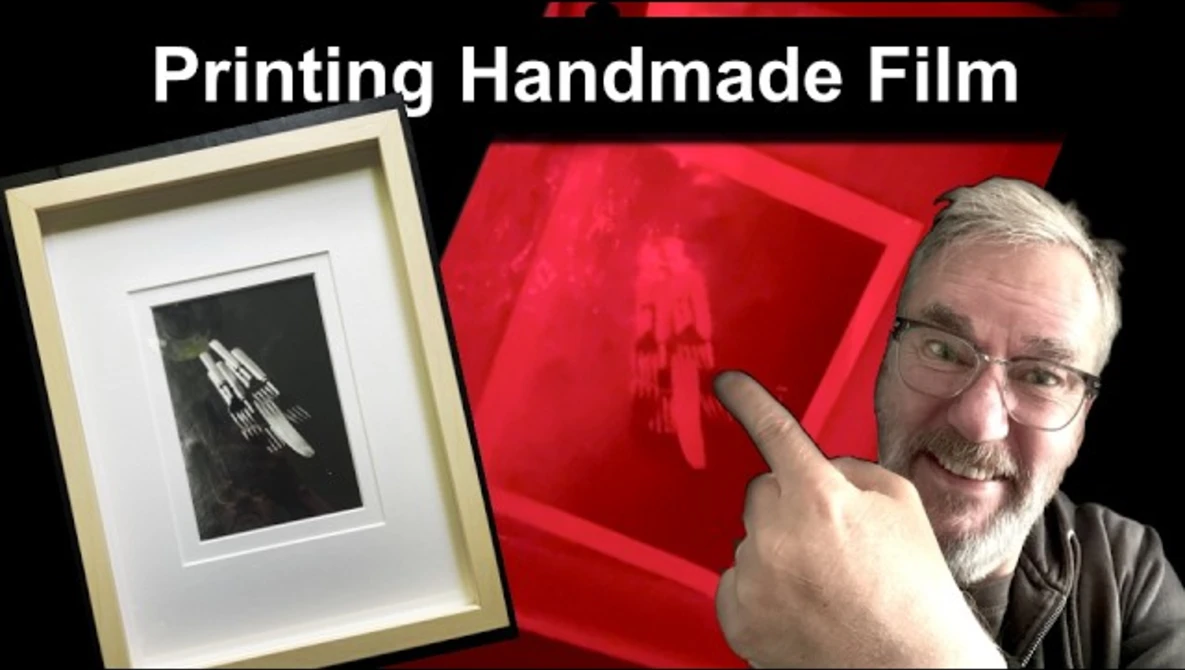 Photographer pointing to framed black and white handmade film print displayed next to red photographic paper