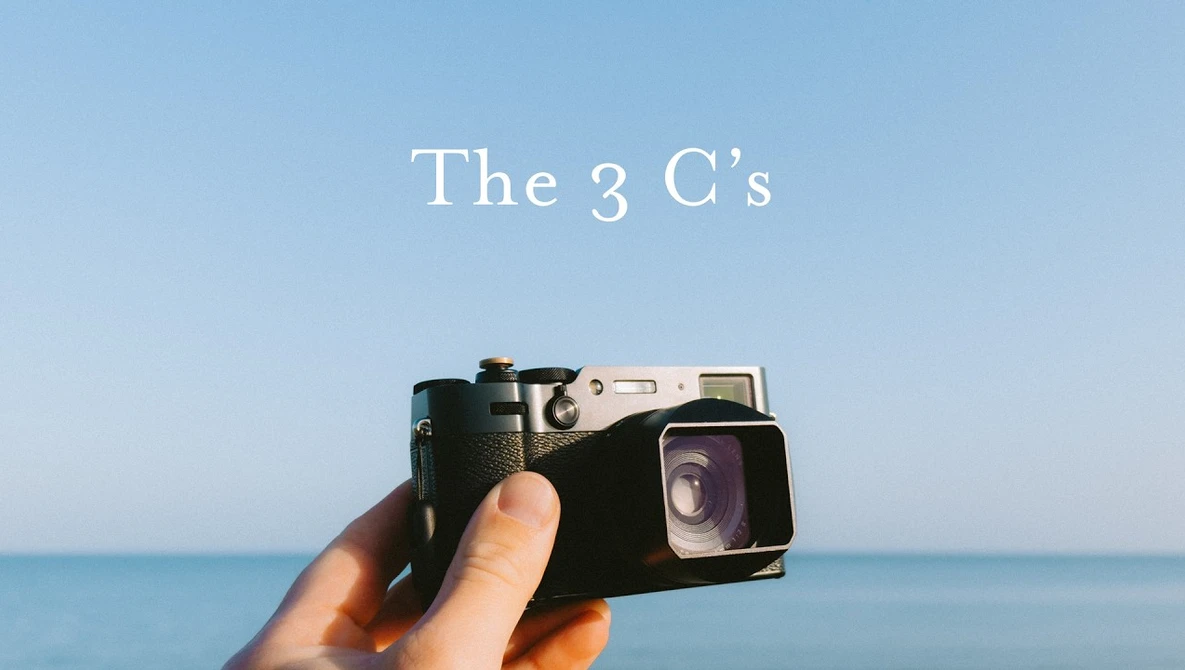 Hand holding a vintage film camera against a clear blue ocean and sky backdrop