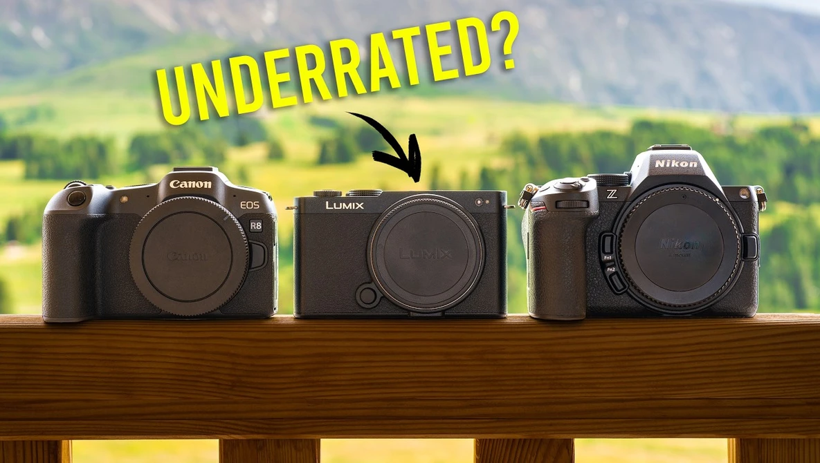 Three mirrorless cameras displayed on wooden rail with scenic countryside backdrop