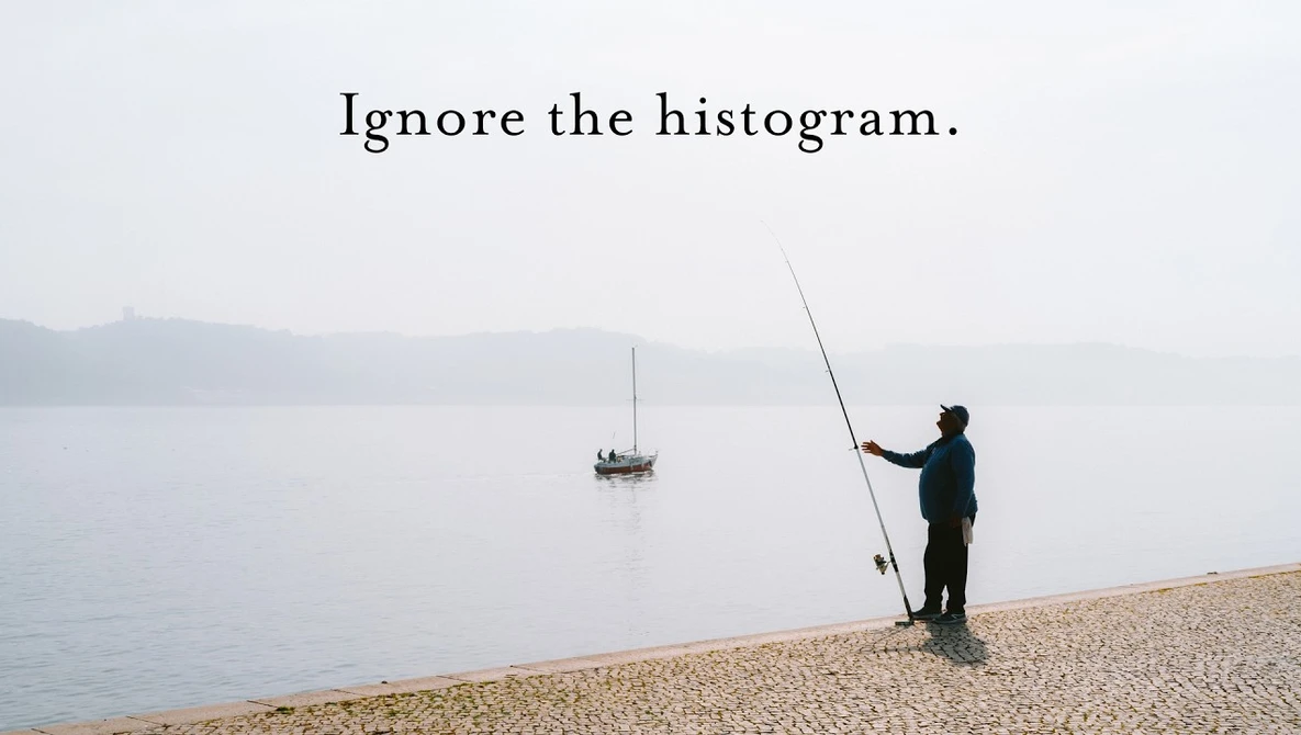 Fisherman casting a line on a misty beach with sailboat in distance