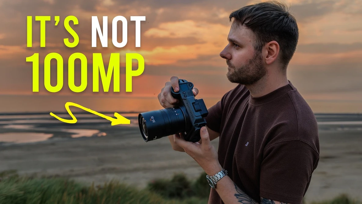 Photographer holding a mirrorless camera with telephoto lens against coastal sunset backdrop