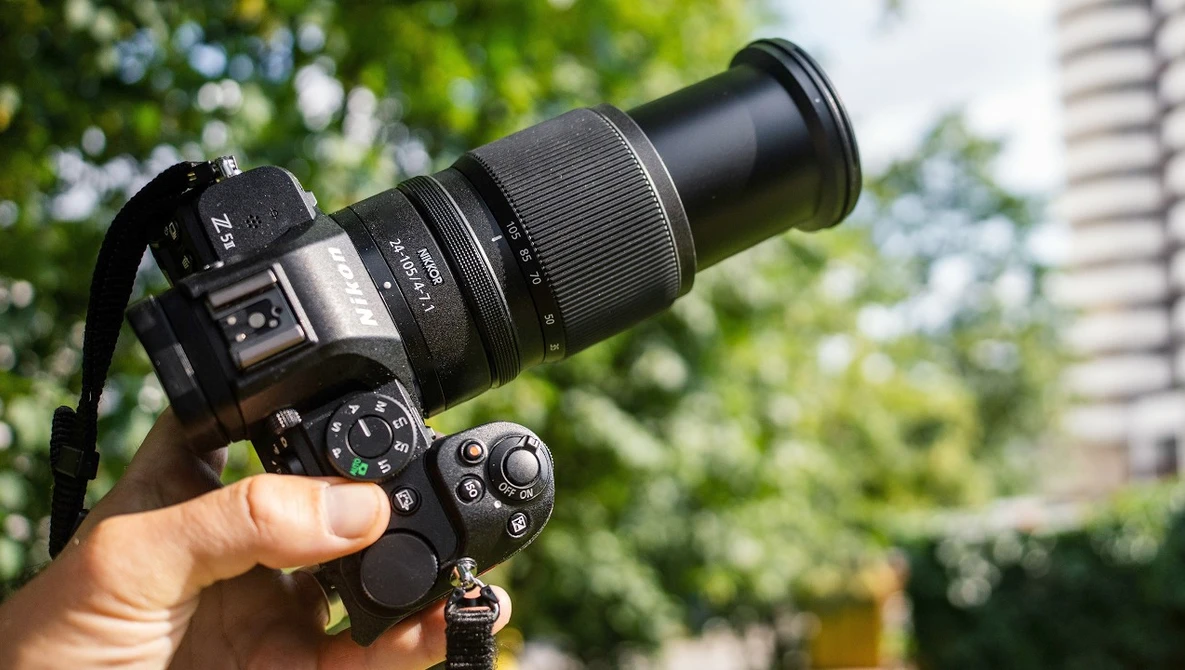 Hand holding a DSLR camera with telephoto lens outdoors in daylight