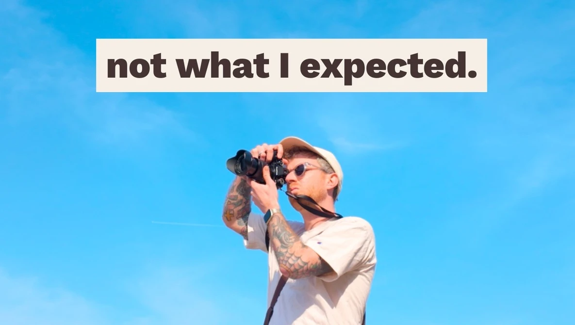 Photographer with camera and sunglasses against blue sky, with text overlay reading 'not what I expected'