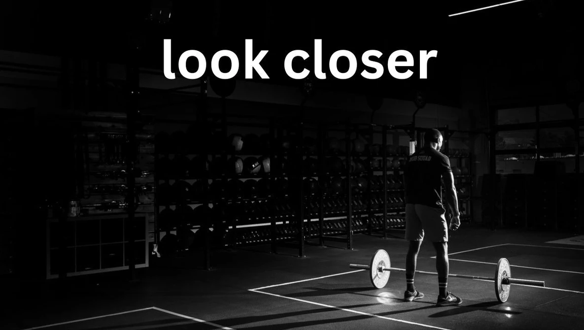 Man in dark suit standing with barbell weights in a minimalist gym space