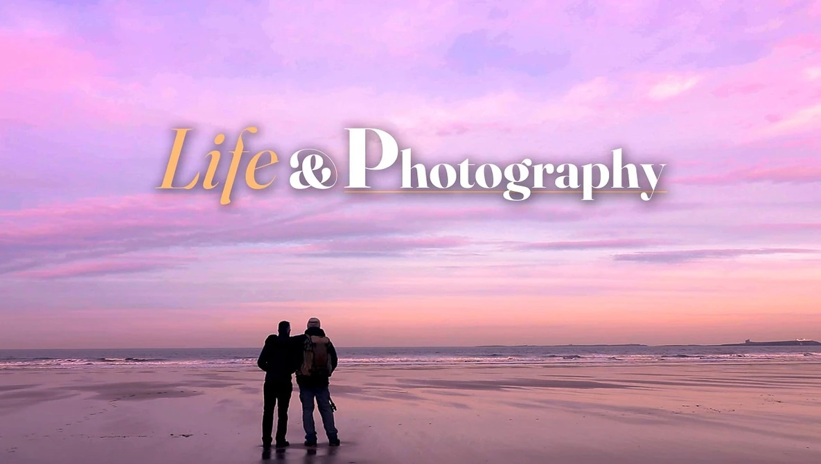 Two silhouetted figures standing on a beach at sunset with pink and purple sky