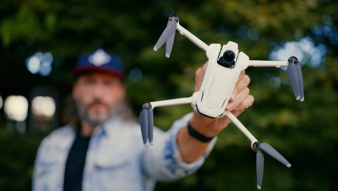 Man holding a white compact drone with extended arms in an outdoor setting