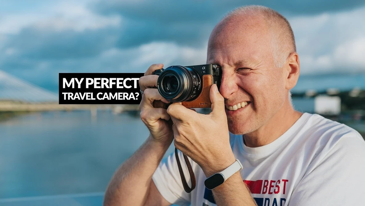 Photographer holding mirrorless camera to eye with water landscape and sky behind