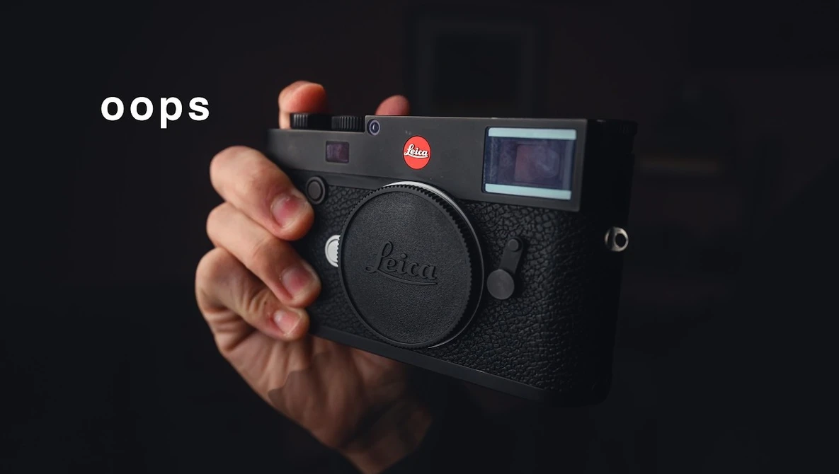 Hand holding a Leica M camera with flash attachment against dark background
