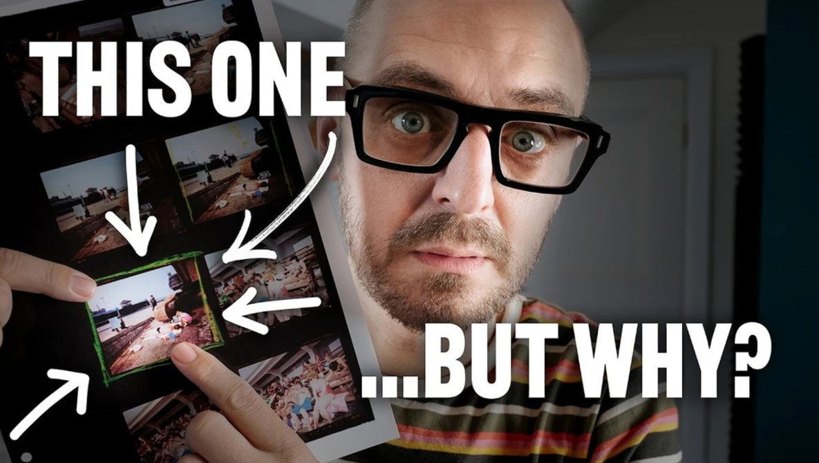 Man with glasses holding multiple printed photographs, pointing at one with a questioning expression