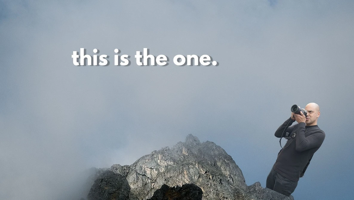 Photographer with telephoto lens photographing a dramatic rocky mountain peak shrouded in mist