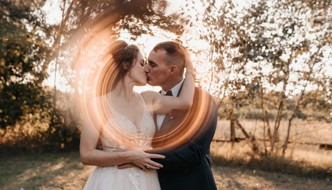 Bride and groom kissing outdoors with a glowing light streak effect around them.
