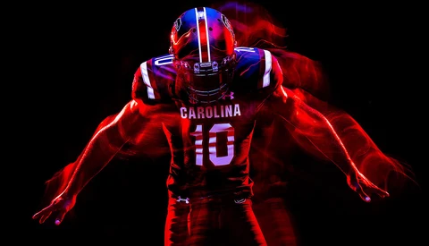 University of South Carolina football player wearing number 10 red jersey, photographed against black background with dramatic red and blue neon lighting effects.