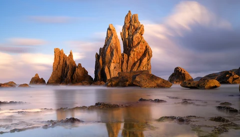 Dramatic rocky sea stacks rising from shallow water at golden hour with smooth water effect.