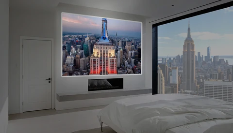 Modern bedroom with large window overlooking city skyline and illuminated art print of iconic skyscraper on white wall.