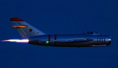 Soviet-era fighter jet in flight with afterburner engaged against deep blue sky