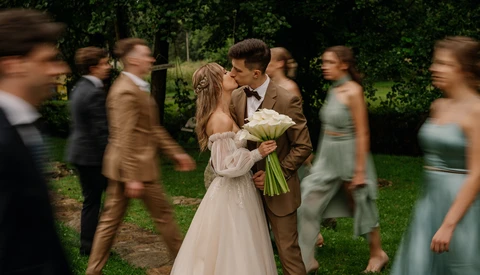 Bride and groom kissing during outdoor garden wedding ceremony surrounded by guests.