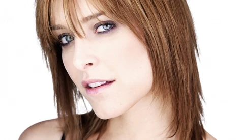 Woman with shoulder-length brown hair and bangs looking at camera against white background.