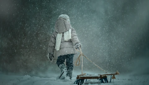 Person in winter clothing pulling a wooden sled through heavy snowfall.