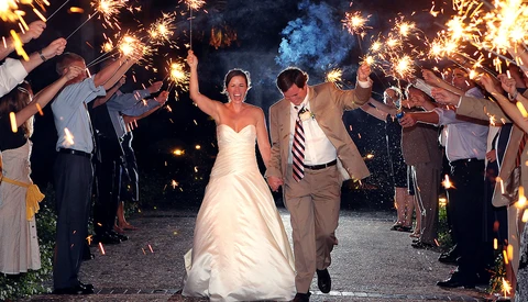 Bride and groom walk through a tunnel of sparklers held by wedding guests at night.